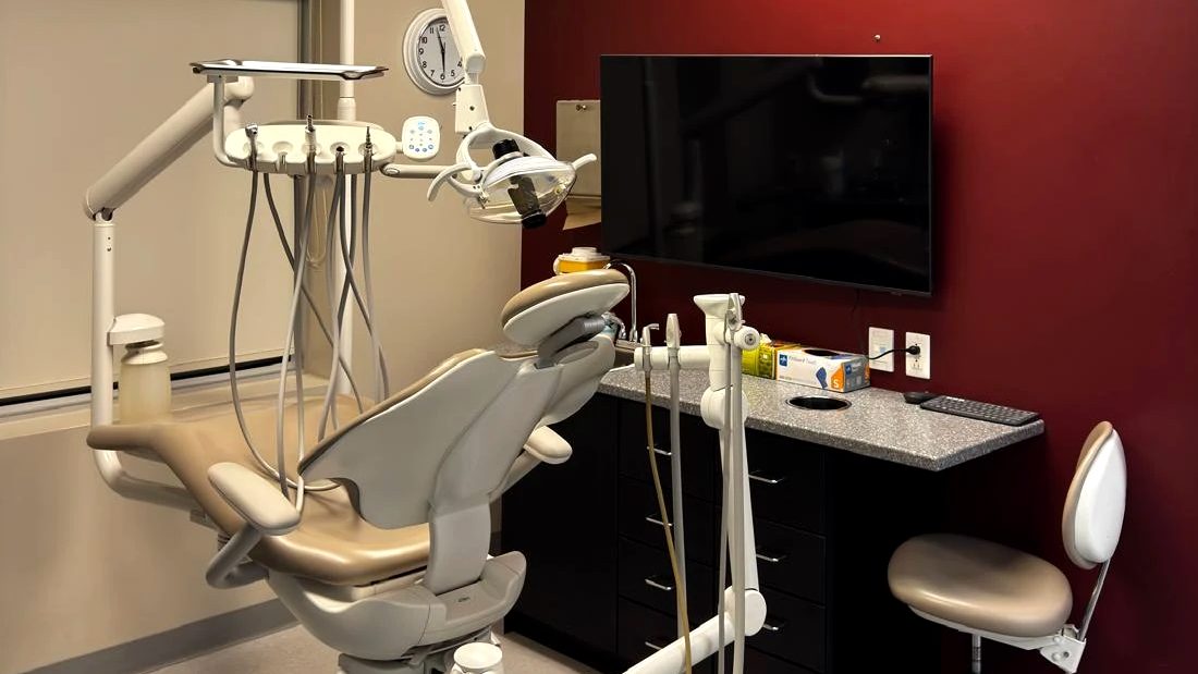 A treatment room at the clinic: a dental chair, a dark red wall and a wall screen